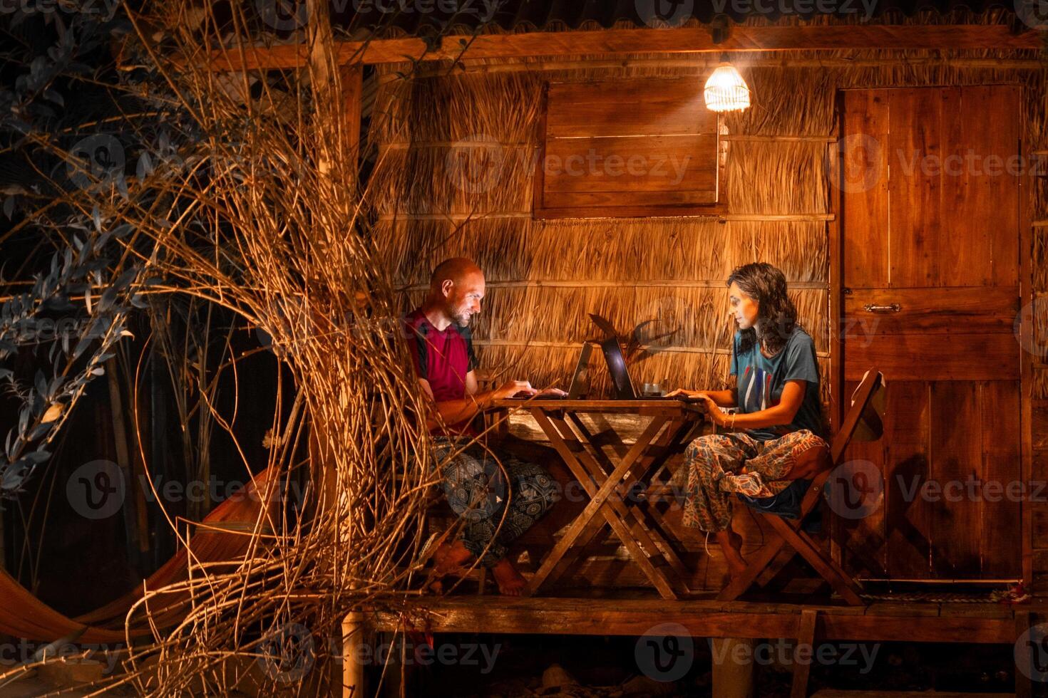 Close up young caucasian hipster couple sit use computer freelance do freelancing work, write travel blog or browse internet search, work online while traveling in southeast asia tropical islands photo