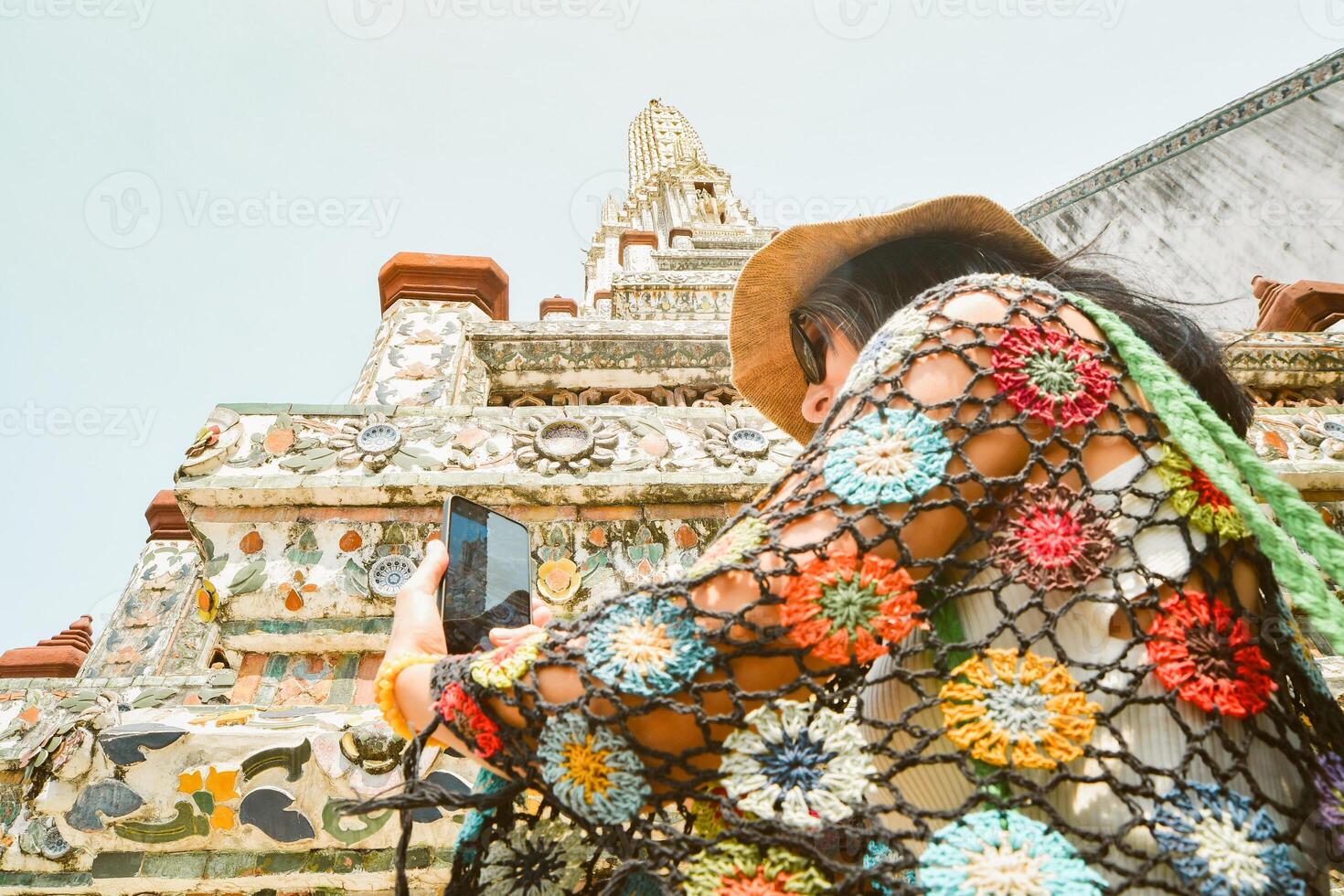 Close up woman tourist taking photo using mobile phone by beautiful Wat Arun temple in Bangkok, Thailand. Famous tourist destination content creator concept post social media