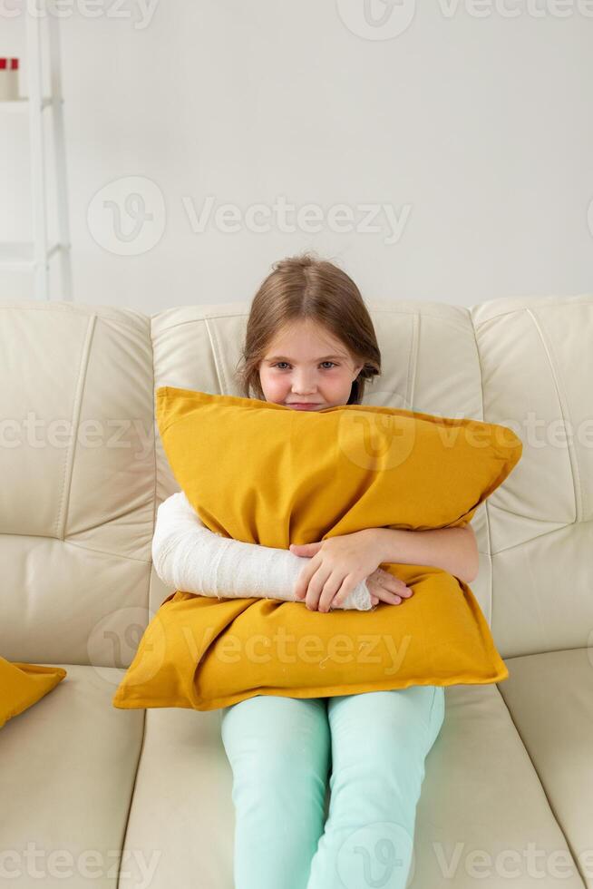 Child with a cast on a broken wrist or arm sitting on a couch. Recovery and disease concept. photo
