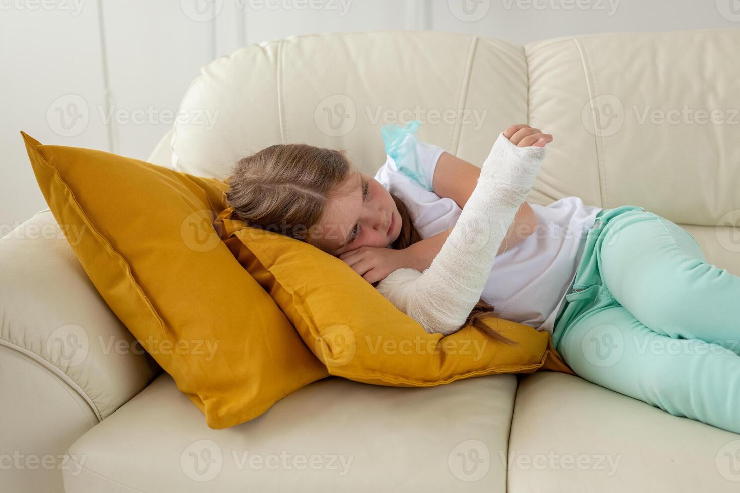 Child with a cast on a broken wrist or arm lying on a couch. Recovery and disease concept. photo