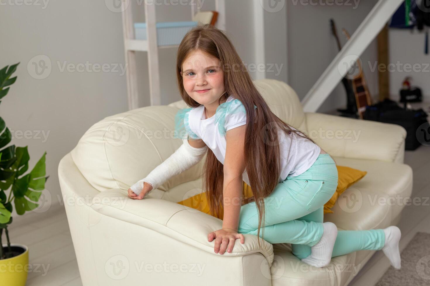 Child with a cast on a broken wrist or arm smiling and having fun on a couch. Positive attitude, recovery and kid concept. photo