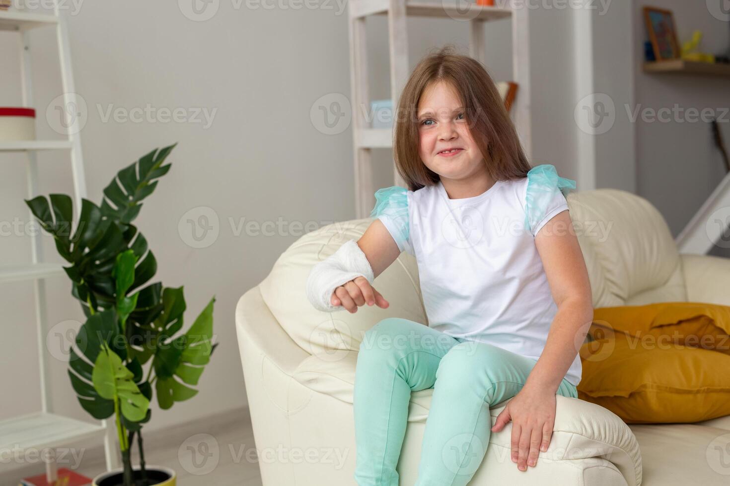 Child with a cast on a broken wrist or arm smiling and having fun on a couch. Positive attitude, recovery and kid concept. photo