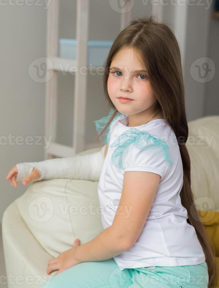 Child with a cast on a broken wrist or arm sits on a couch. Recovery and kid concept. photo