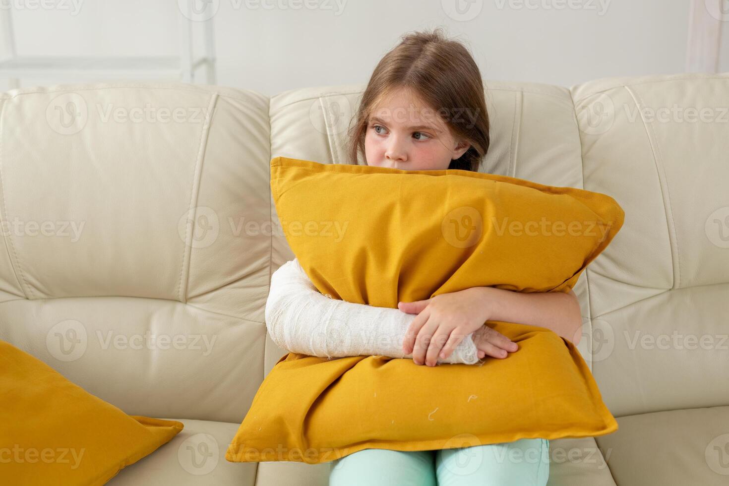 Child with a cast on a broken wrist or arm sitting on a couch. Recovery and disease concept. photo