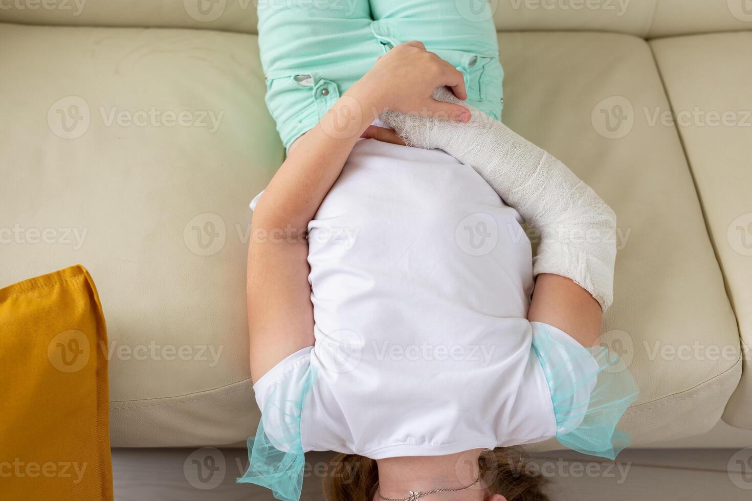Child with a cast on a broken wrist or arm smiling and having fun on a couch. Positive attitude, recovery and kid concept. photo