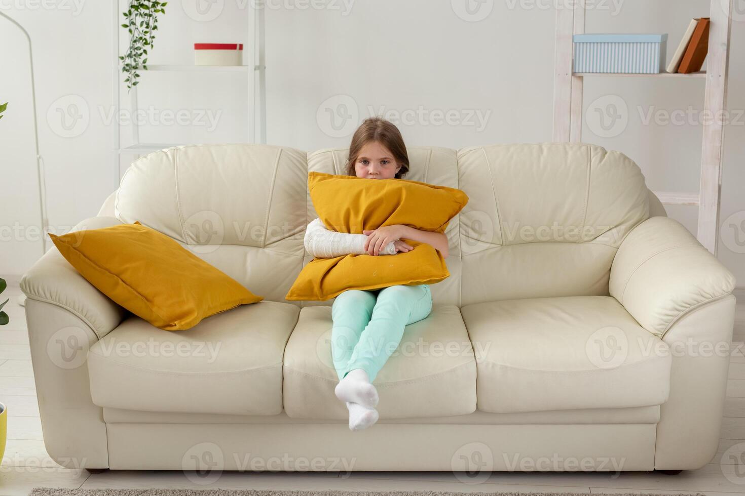 Child with a cast on a broken wrist or arm sitting on a couch. Recovery and disease concept. photo