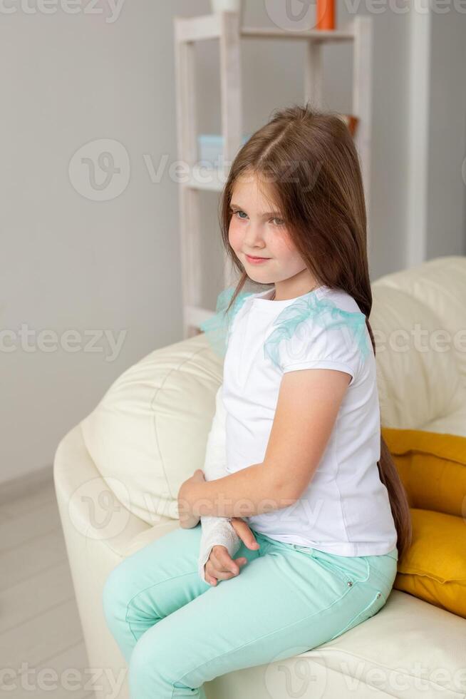 Child with a cast on a broken wrist or arm smiling and having fun on a couch. Positive attitude, recovery and kid concept. photo