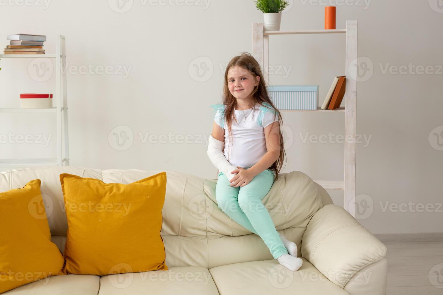 Child with a cast on a broken wrist or arm smiling and having fun on a couch. Positive attitude, recovery and kid concept. photo