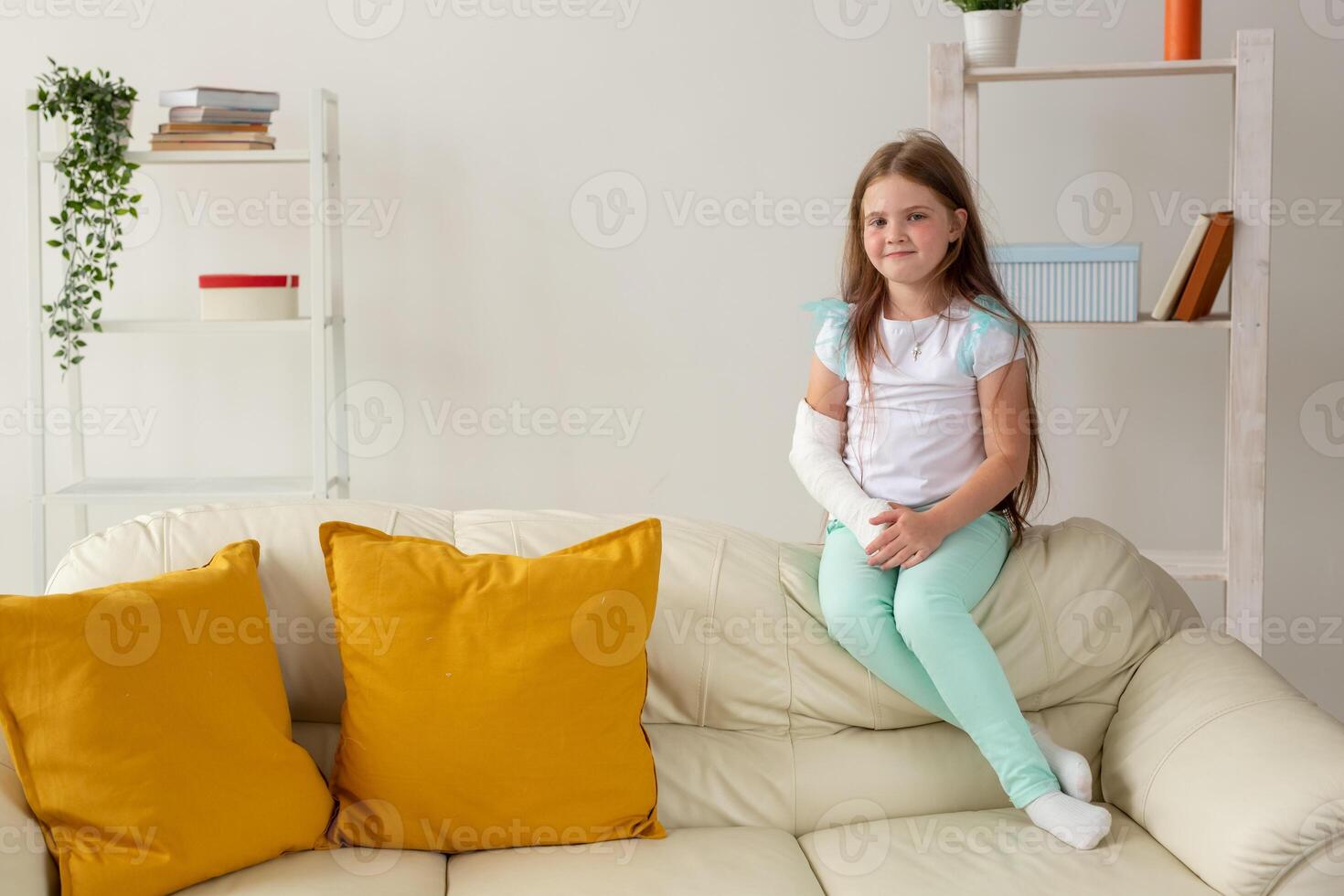 Child with a cast on a broken wrist or arm smiling and having fun on a couch. Positive attitude, recovery and kid concept. photo