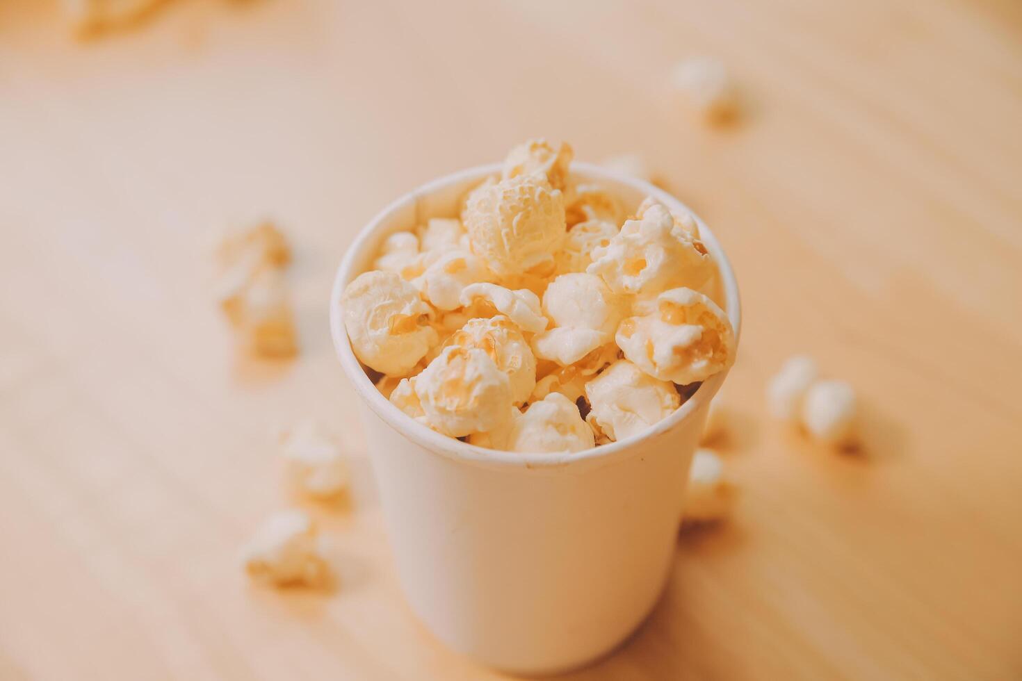 A bucket of popcorn, top-view, warm colors, light brown wooden background, flat lay, daylight macro close-up photo