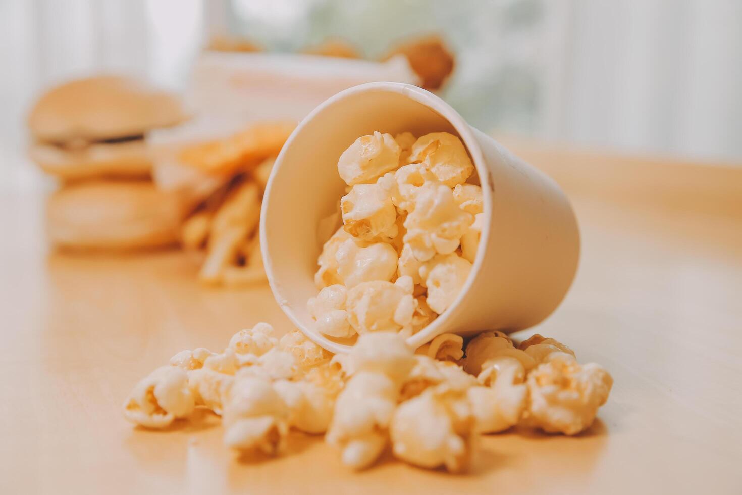 A bucket of popcorn, top-view, warm colors, light brown wooden background, flat lay, daylight macro close-up photo