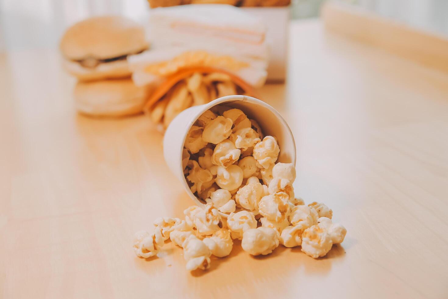 A bucket of popcorn, top-view, warm colors, light brown wooden background, flat lay, daylight macro close-up photo