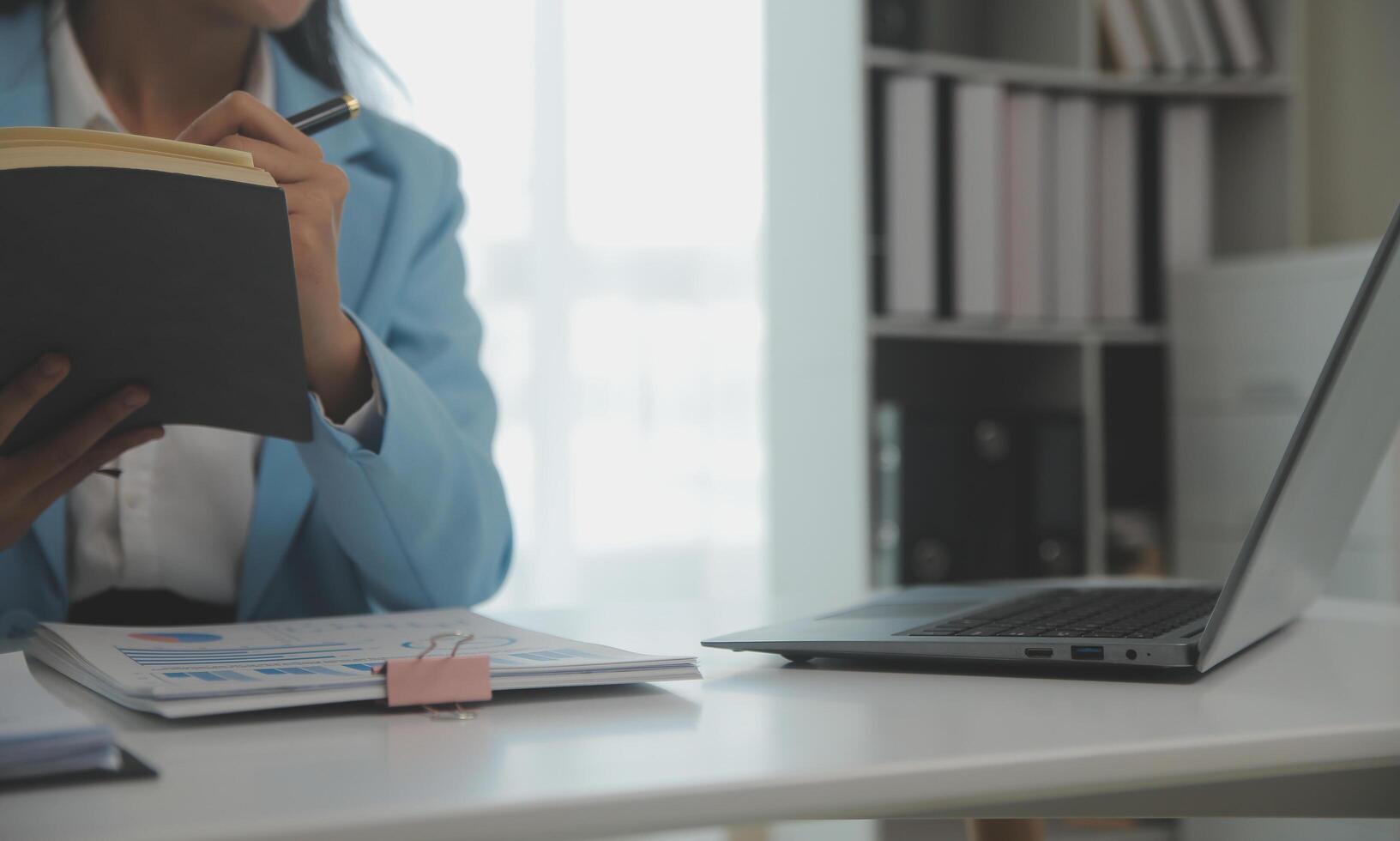 Charming Young asian businesswoman sitting on laptop computer in the office, making report calculating balance Internal Revenue Service checking document. photo