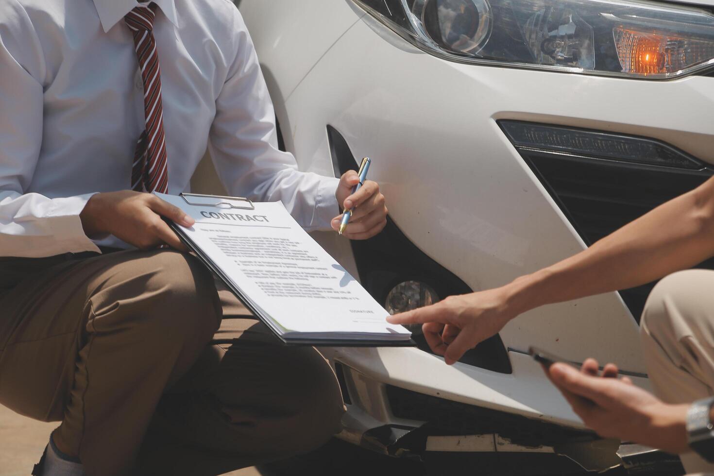 Side view of writing on clipboard while insurance agent examining car after accident photo