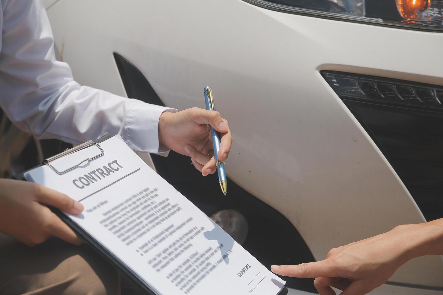 Side view of writing on clipboard while insurance agent examining car after accident photo