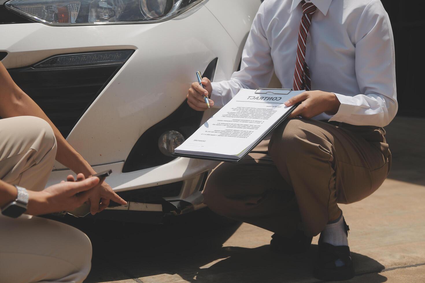Side view of writing on clipboard while insurance agent examining car after accident photo