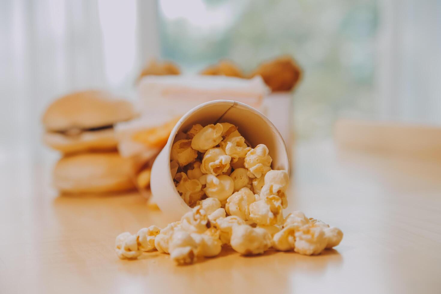 A bucket of popcorn, top-view, warm colors, light brown wooden background, flat lay, daylight macro close-up photo