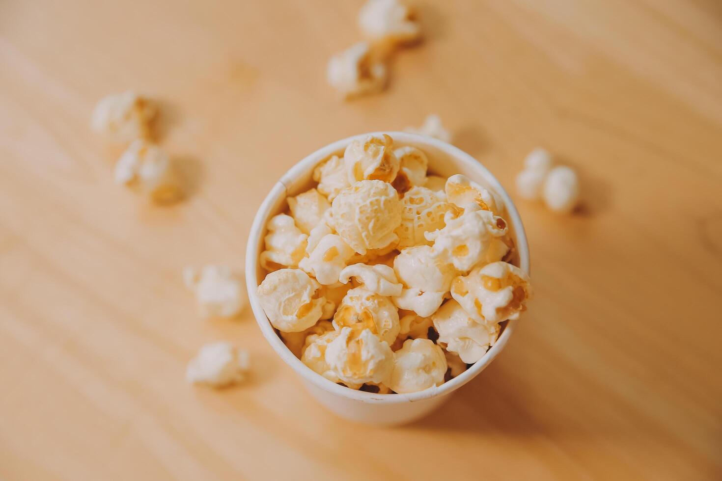 A bucket of popcorn, top-view, warm colors, light brown wooden background, flat lay, daylight macro close-up photo
