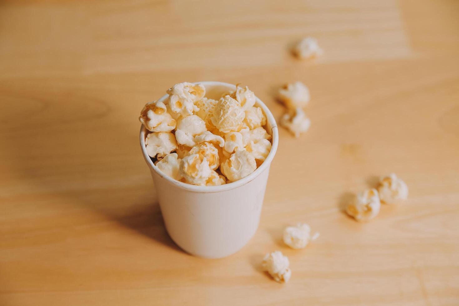 A bucket of popcorn, top-view, warm colors, light brown wooden background, flat lay, daylight macro close-up photo