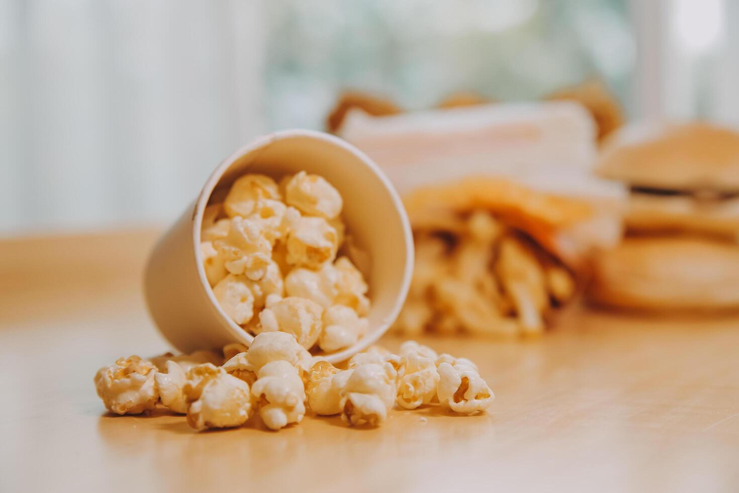 A bucket of popcorn, top-view, warm colors, light brown wooden background, flat lay, daylight macro close-up photo