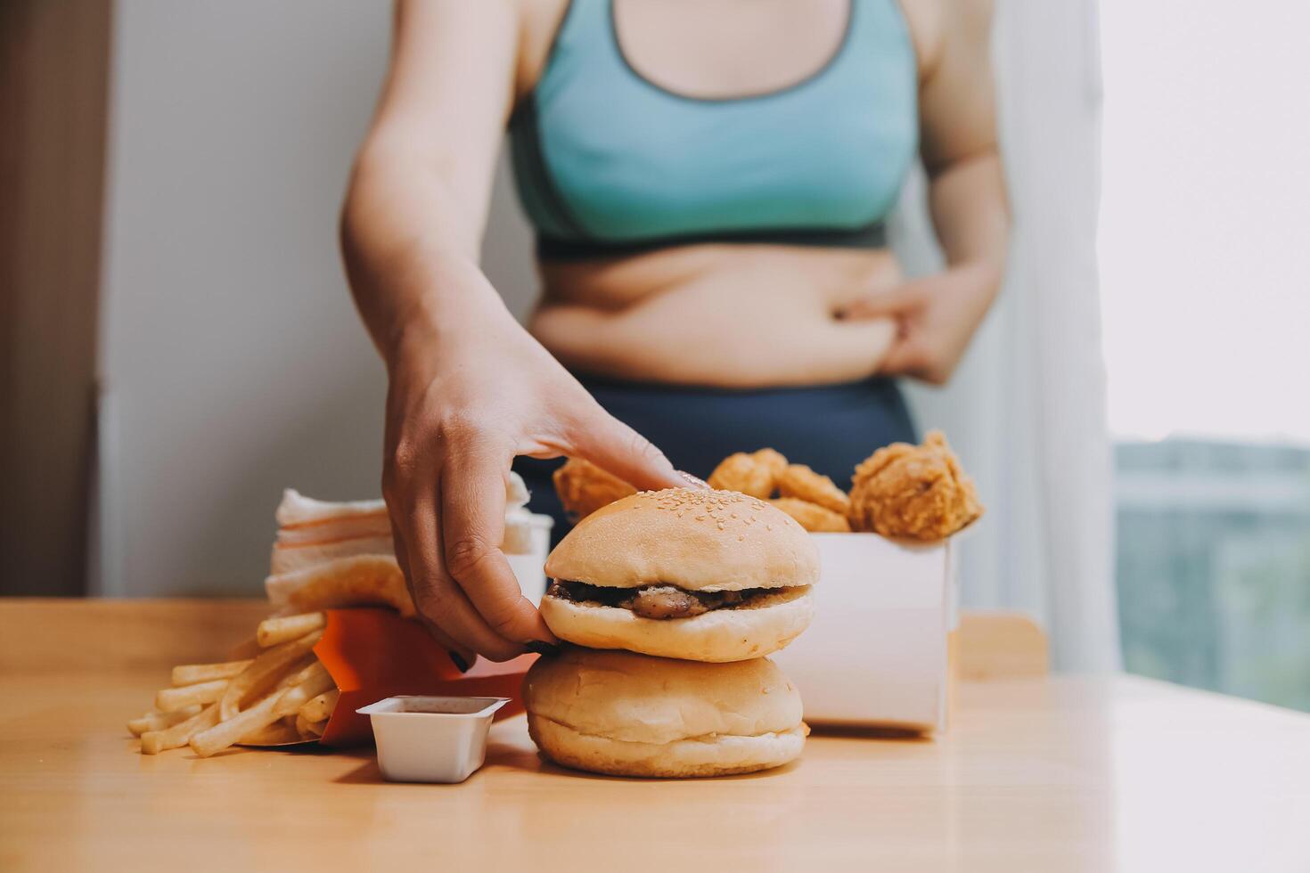 To eat or not. Cheerless plump woman looking at the burger while thinking to eat it or not photo