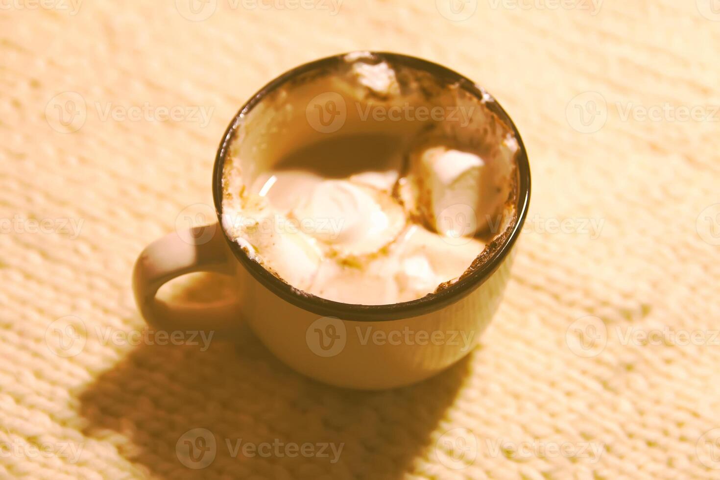 Hot fresh cocoa drink in a ceramic mug with melting sweet marshmallows on cozy knitted background photo