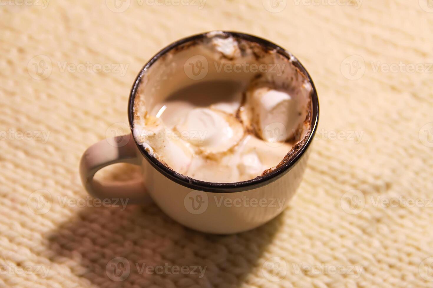 Hot fresh cocoa drink in a ceramic mug with melting sweet marshmallows on cozy knitted background photo