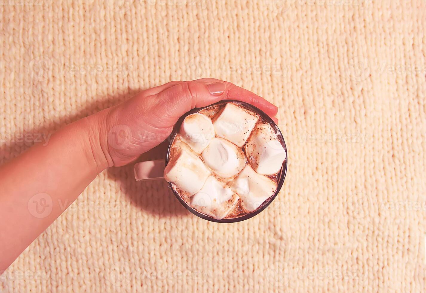 Woman's hand holding ceramic mug with hot fresh cocoa drink with marshmallows photo