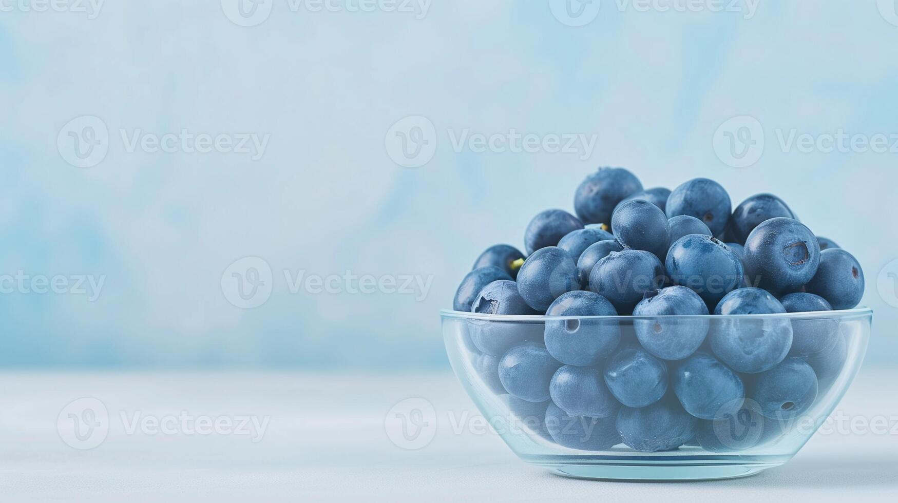Fresh Blueberries in a Clear Glass Bowl on a White Table with Light Blue Gradient Background, Perfect for Healthy Eating, Food Photography, and Nutritional Concepts photo