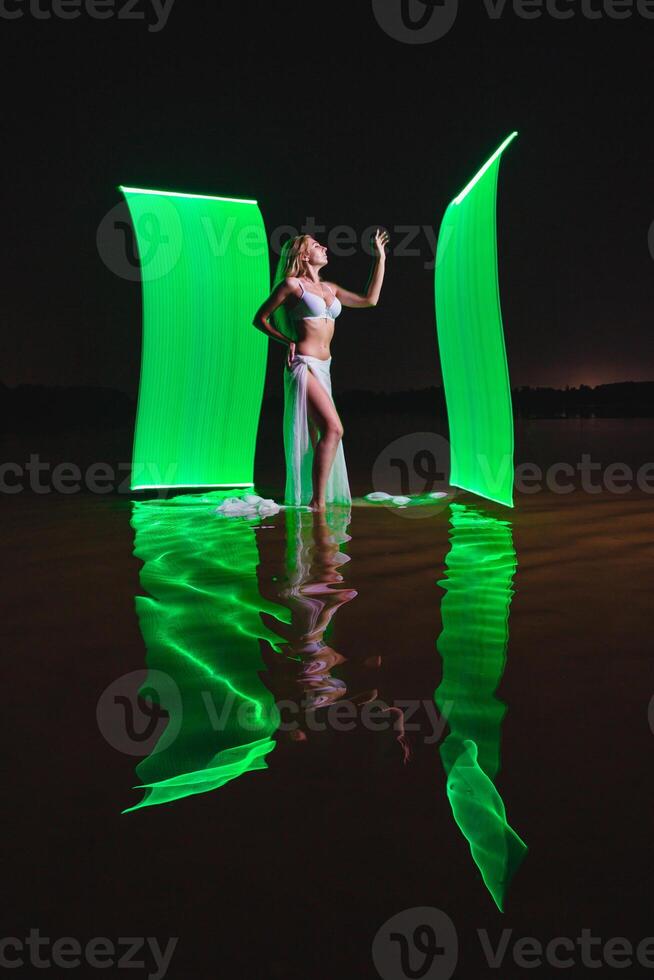 Young slim girl posing in water with abstract green light effect photo