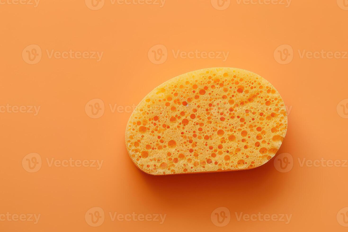 Yellow kitchen sponge on a vibrant orange background photo
