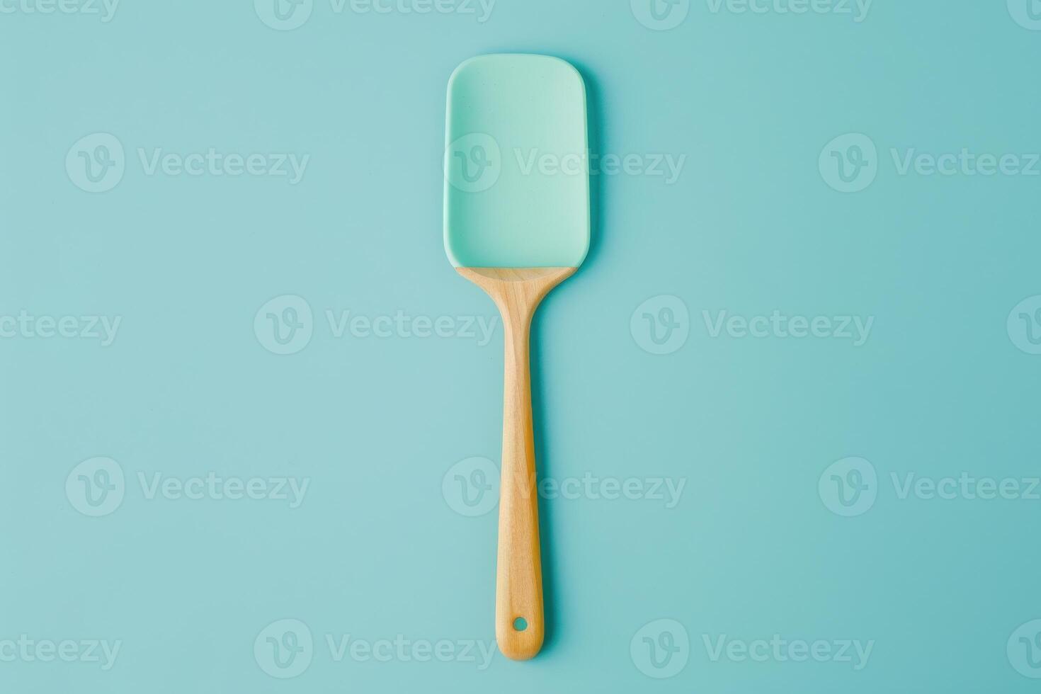 Mint green silicone spatula on a light blue background with wooden handle photo
