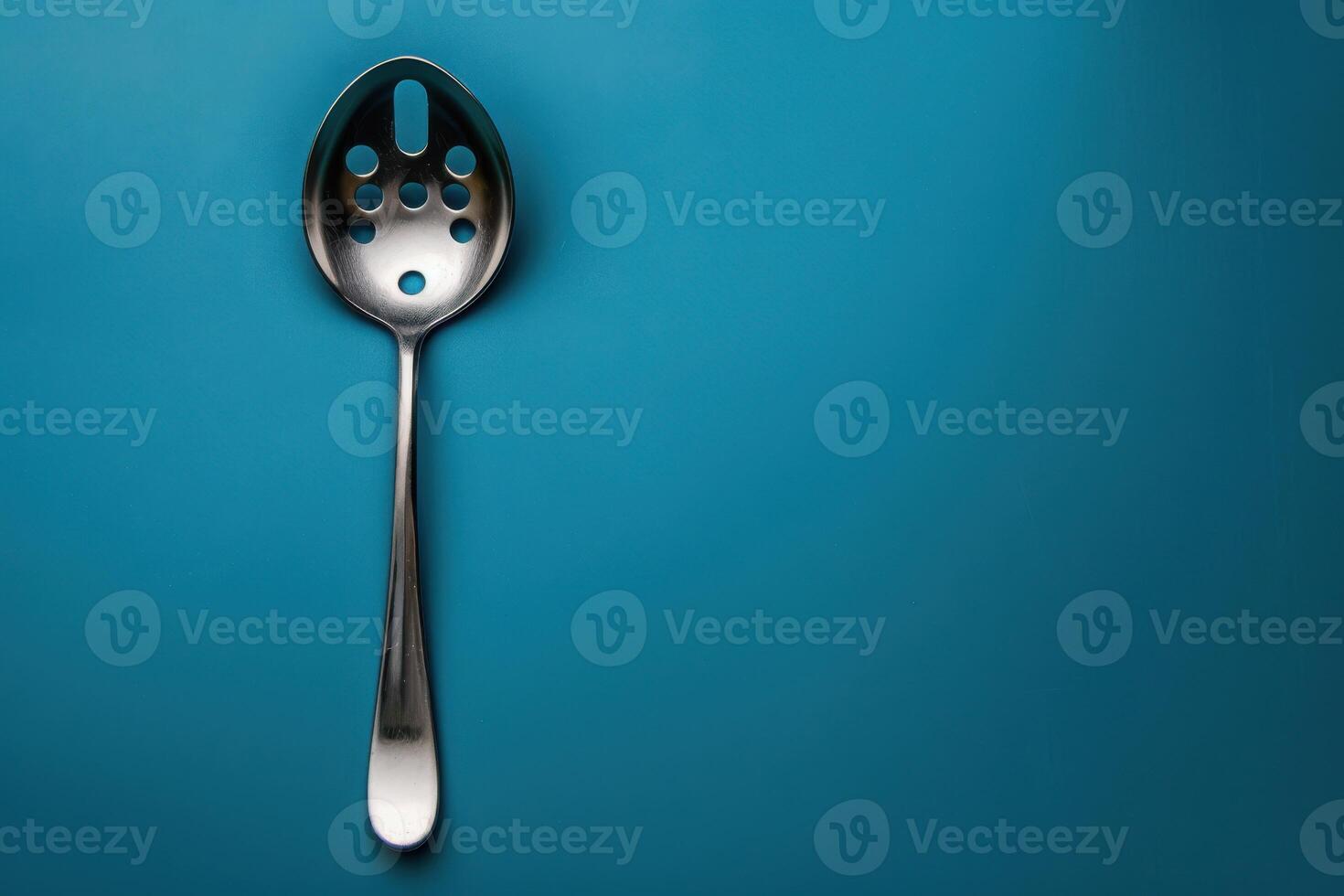 Metal slotted spoon resting on a blue background photo