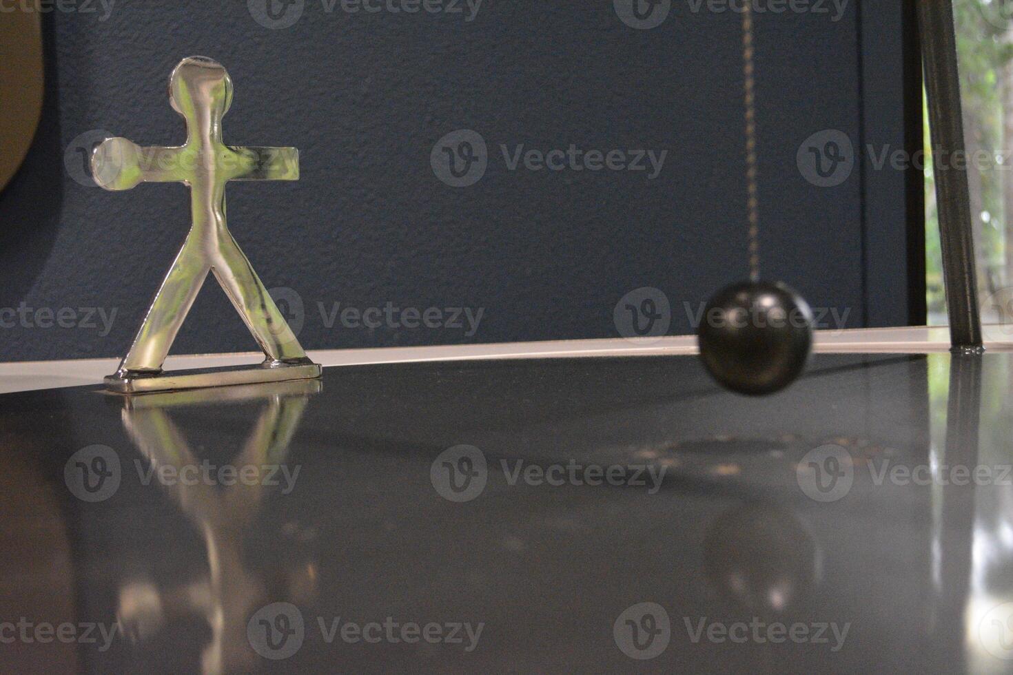 A metal human figure and a pendulum ball near it. The concept of human endurance and resilience in the face of adversity and difficulties. photo