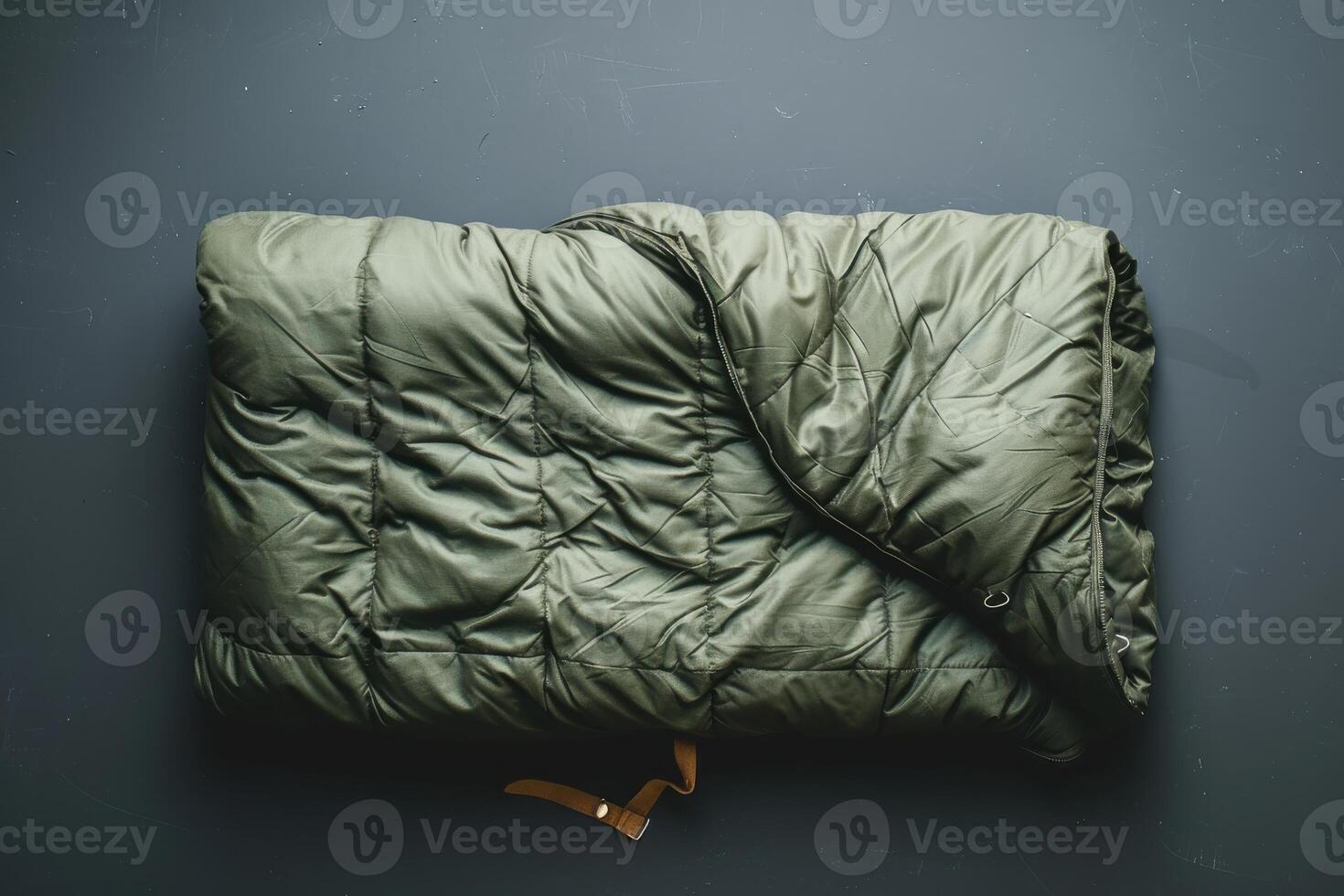 Folded green quilt resting on a dark surface with a brown strap photo