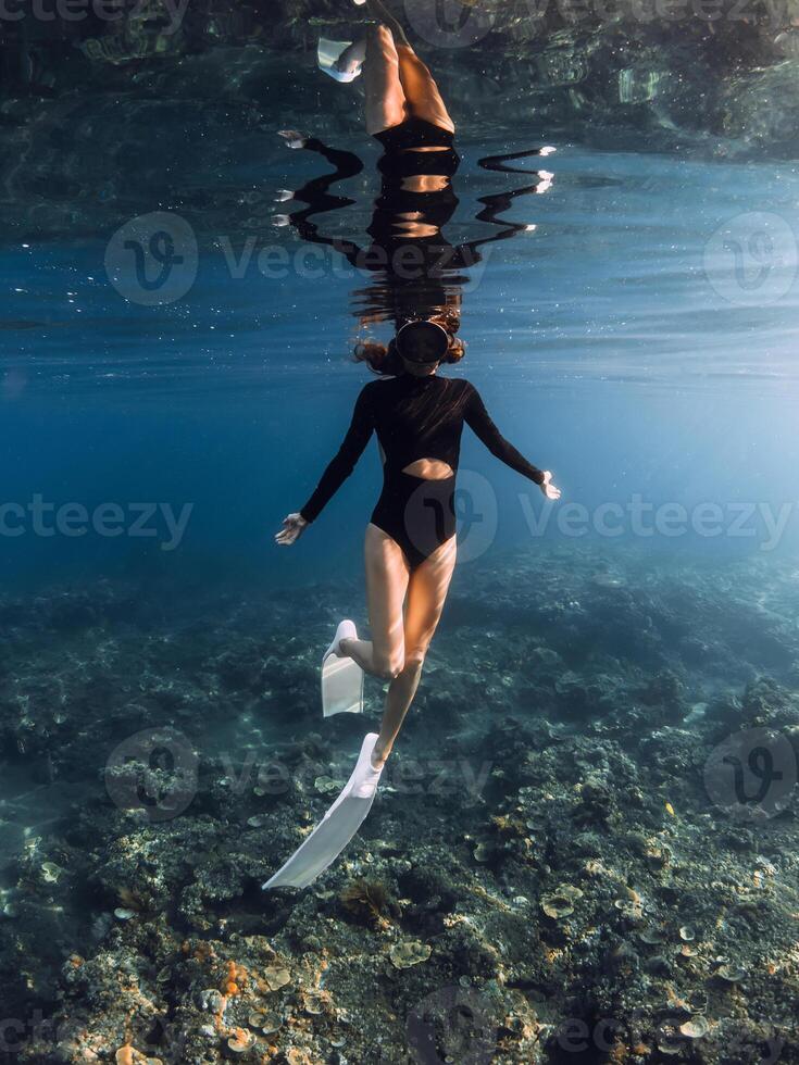 Woman freediver enjoys swimming in blue ocean on the reef. Vertical shot photo