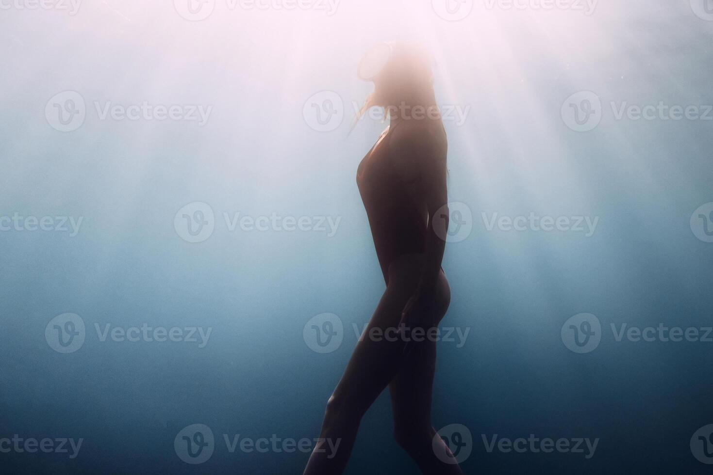 Sexy woman silhouette undersea. Gorgeous freediver swims underwater in deep blue ocean with sunrays. photo