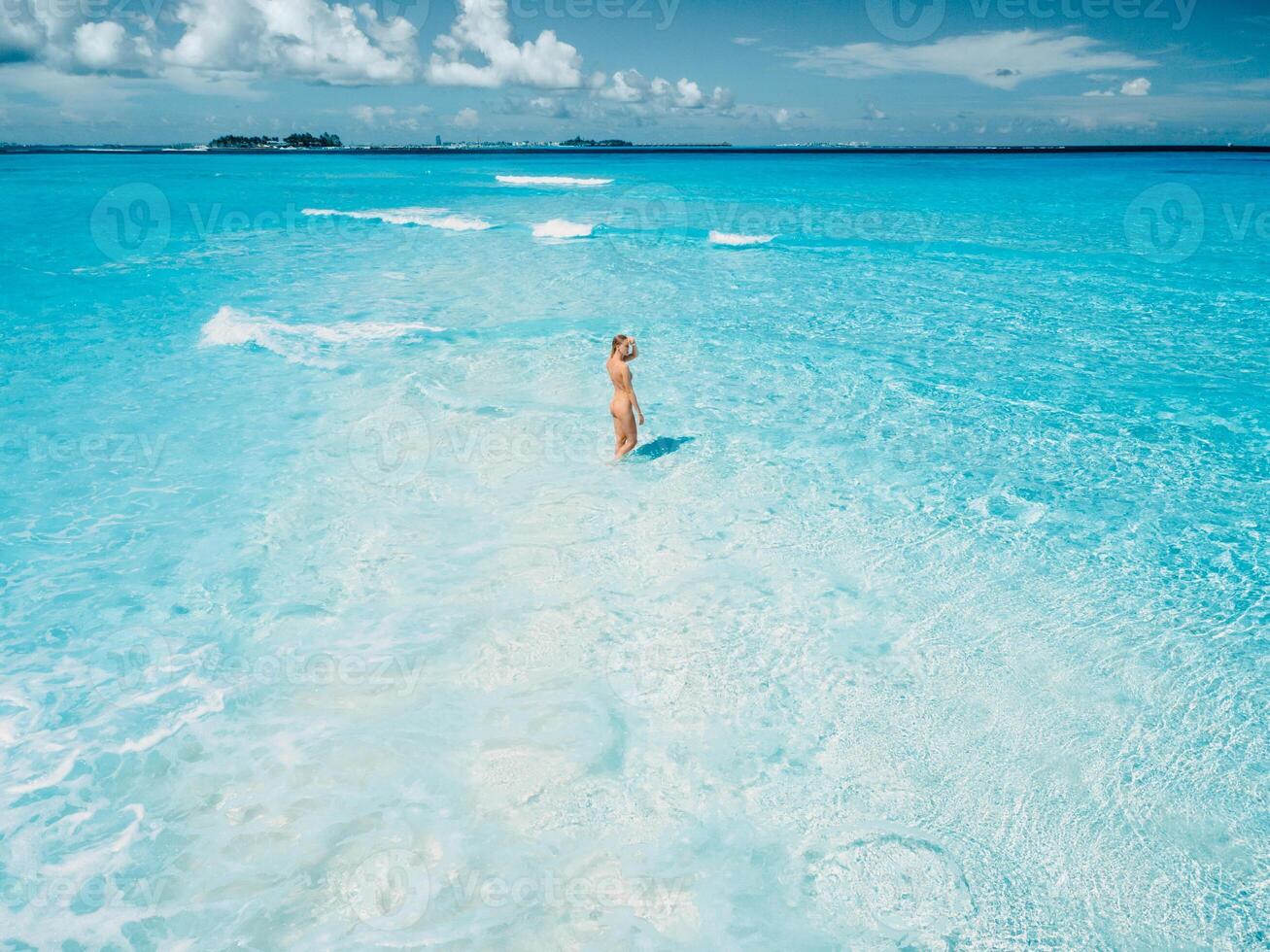 Woman in swimsuit staying on tropical white sandy beach with turquoise ocean water. Drone view photo