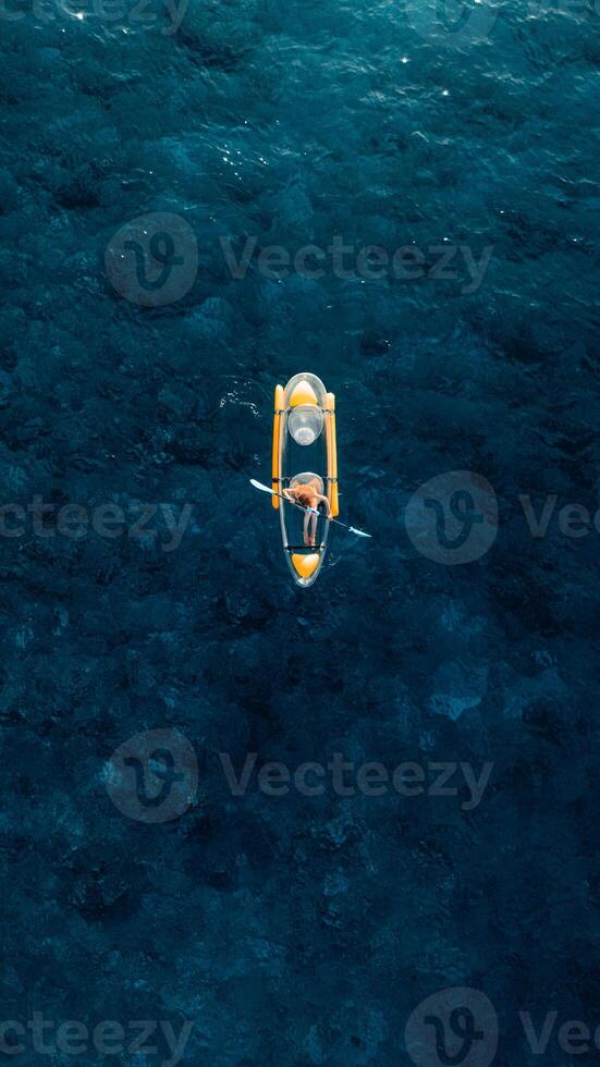 Vertical Screen. Woman rowing on kayak in tropical blue ocean. Drone view photo