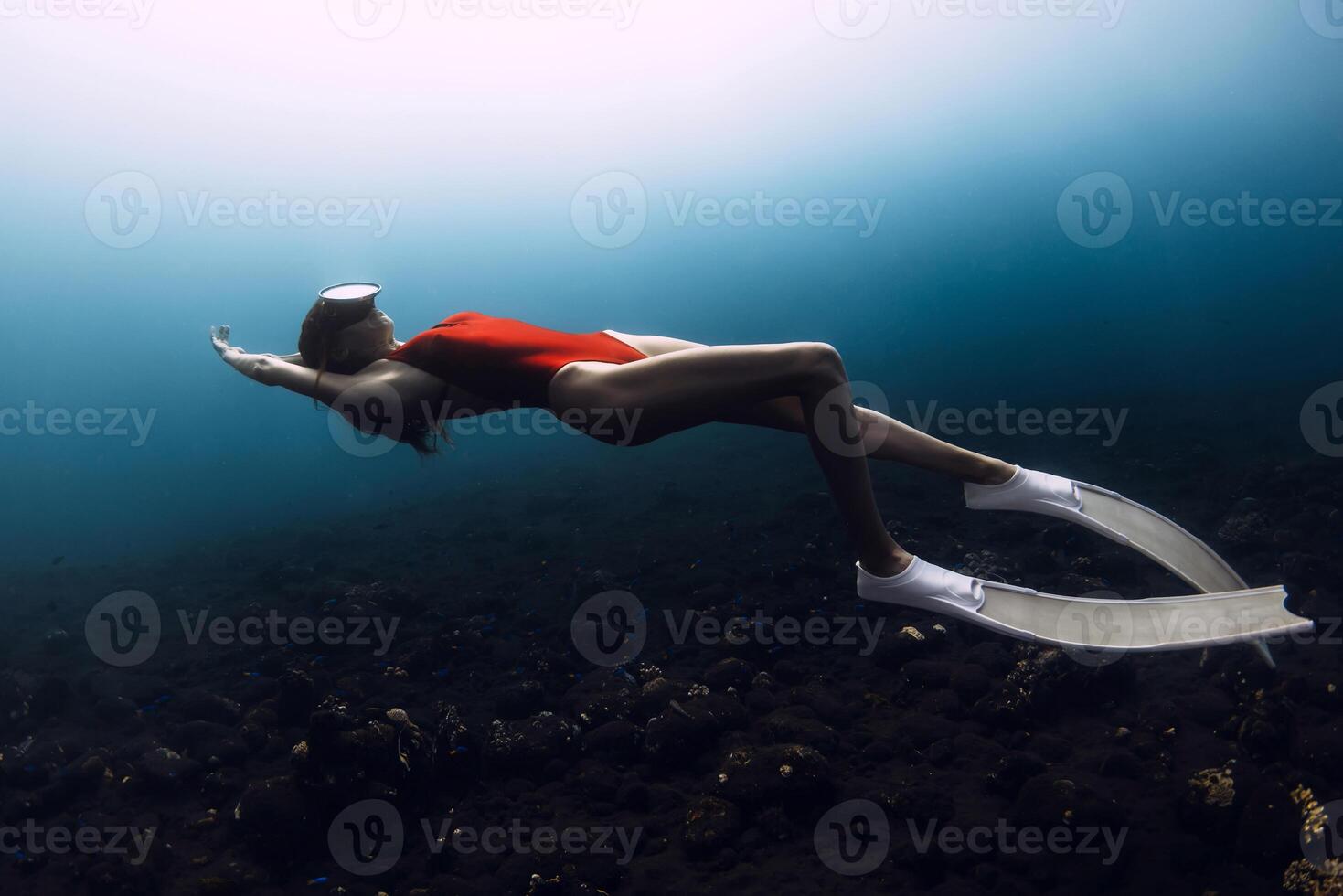 Young gorgeous girl freediver in red swimwear swims underwater in deep blue ocean. photo