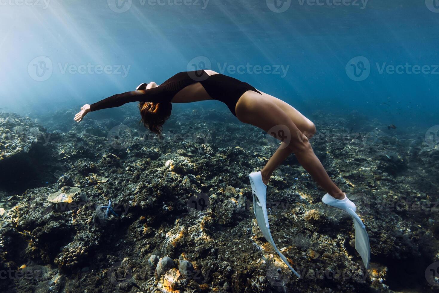 Freediver woman posing over coral reef with sun rays in tropical ocean photo