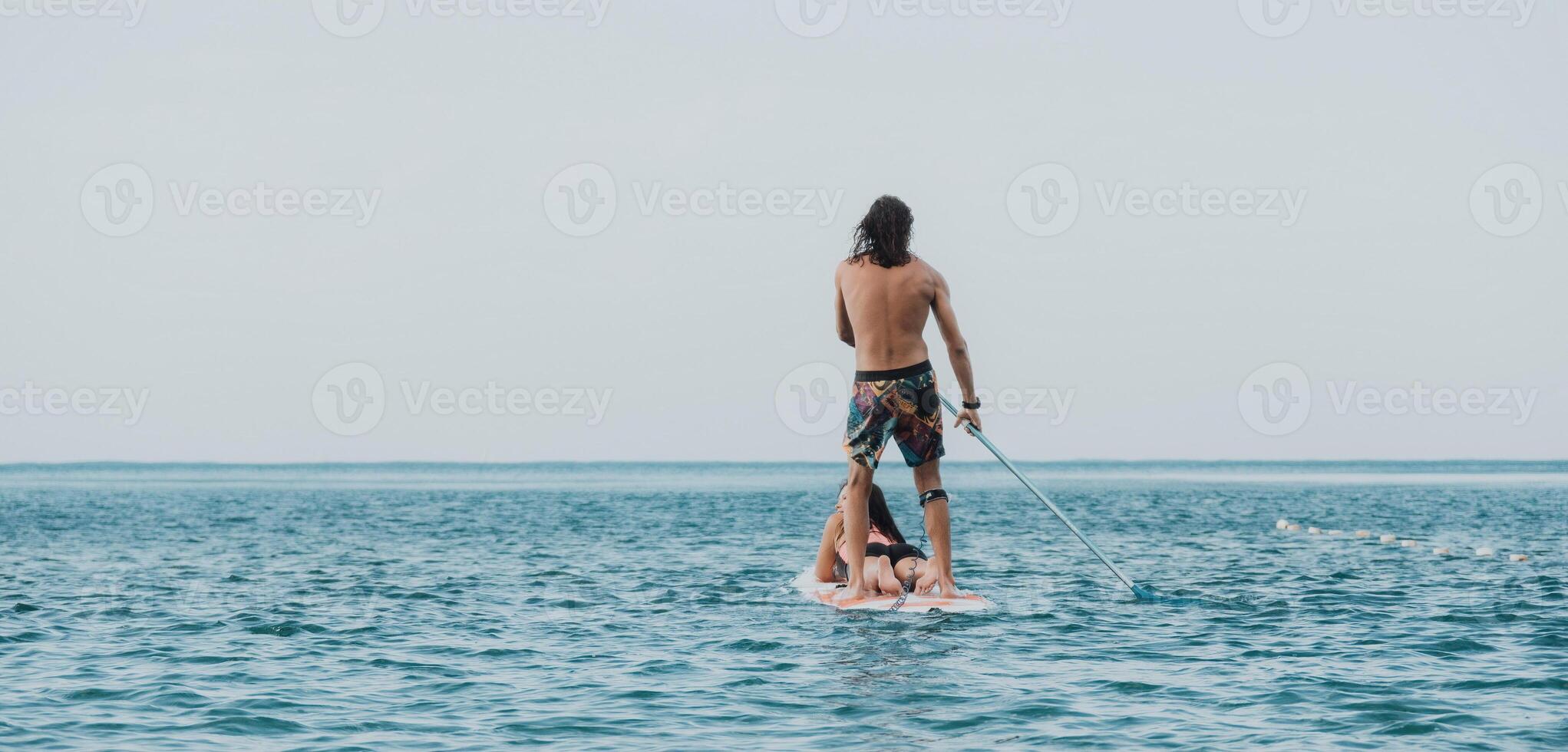 Sea woman and man on sup. Silhouette of happy young woman and man, surfing on SUP board, confident paddling through water surface. Idyllic sunset. Active lifestyle at sea or river. photo