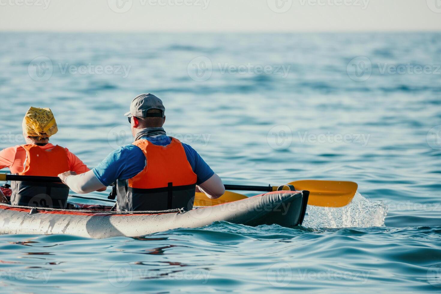 Happy couple kayaks in an inflatable kayak on the sea at sunset. Couple kanoeing in the sea near the island with mountains. People kayaking in life jackets sail. Back view photo