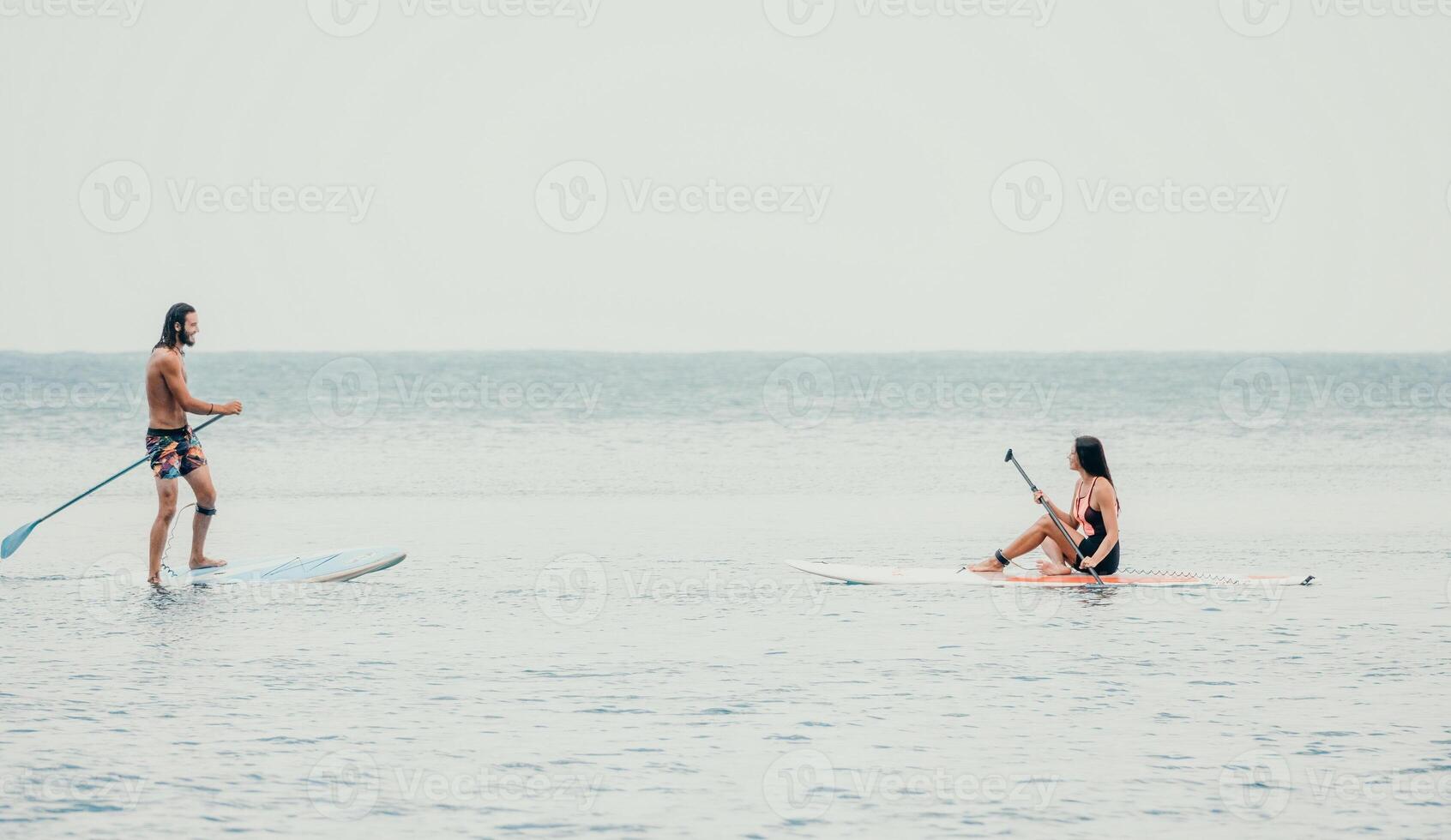 Sea woman and man on sup. Silhouette of happy young woman and man, surfing on SUP board, confident paddling through water surface. Idyllic sunset. Active lifestyle at sea or river. photo