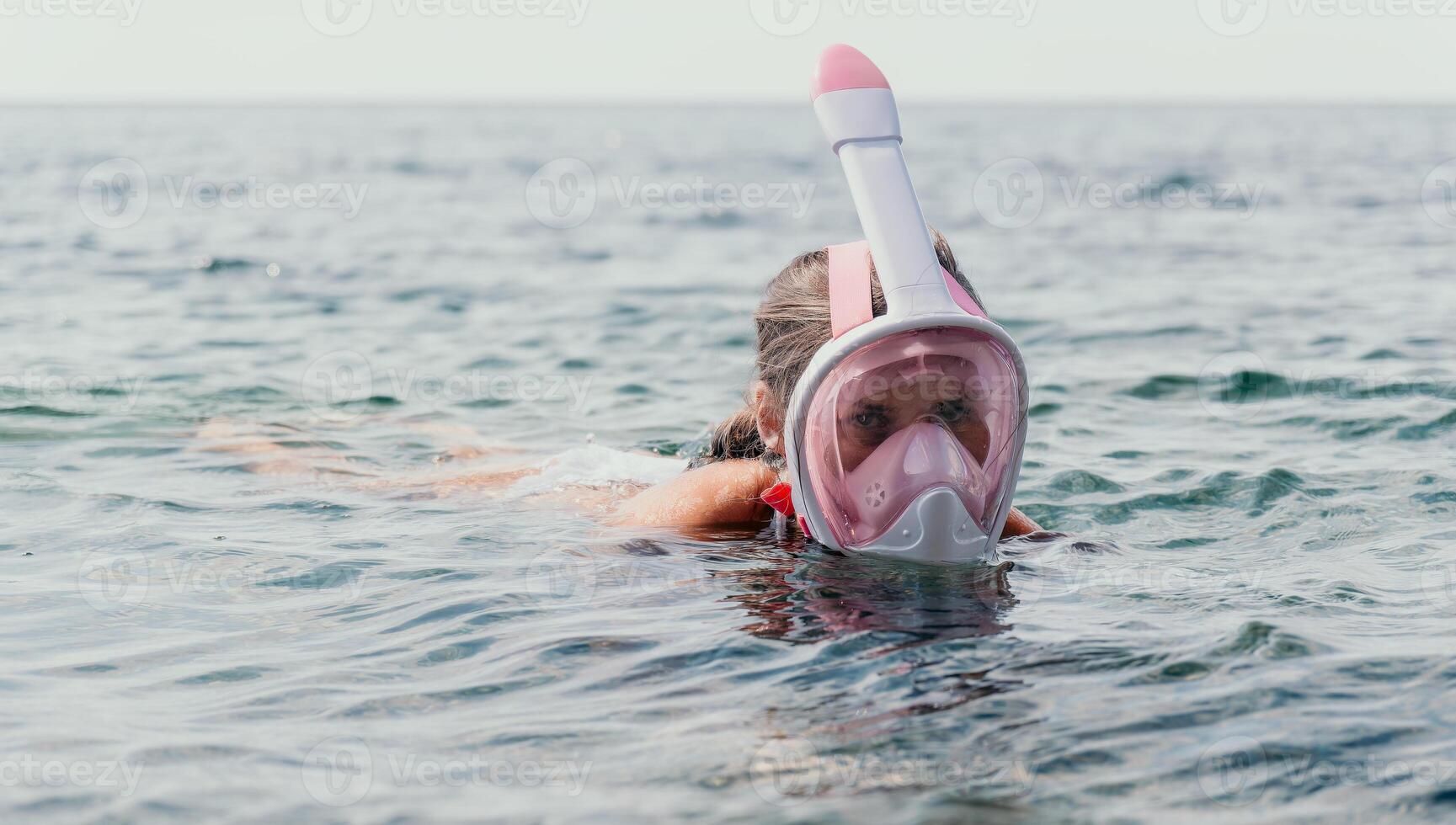 Young happy woman in white bikini and wearing pink mask gets ready for sea snorkeling. Positive smiling woman relaxing and enjoying water activities with family summer travel holidays vacation on sea. photo