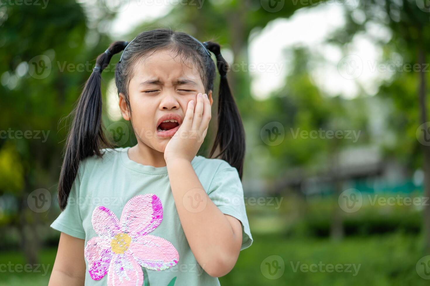 Tooth ache concept. Asian Little girl holding her cheek with hand, suffering from bad toothache. Kid with painful expression .Caries. a loose tooth, Severe tooth pain. photo