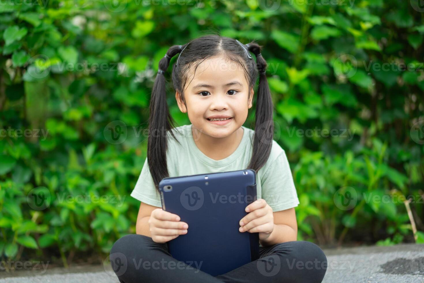 Asian little child girl playing tablet and smartphone happiness. child girl relaxing at the Park. Play tablet and smartphone concept. photo