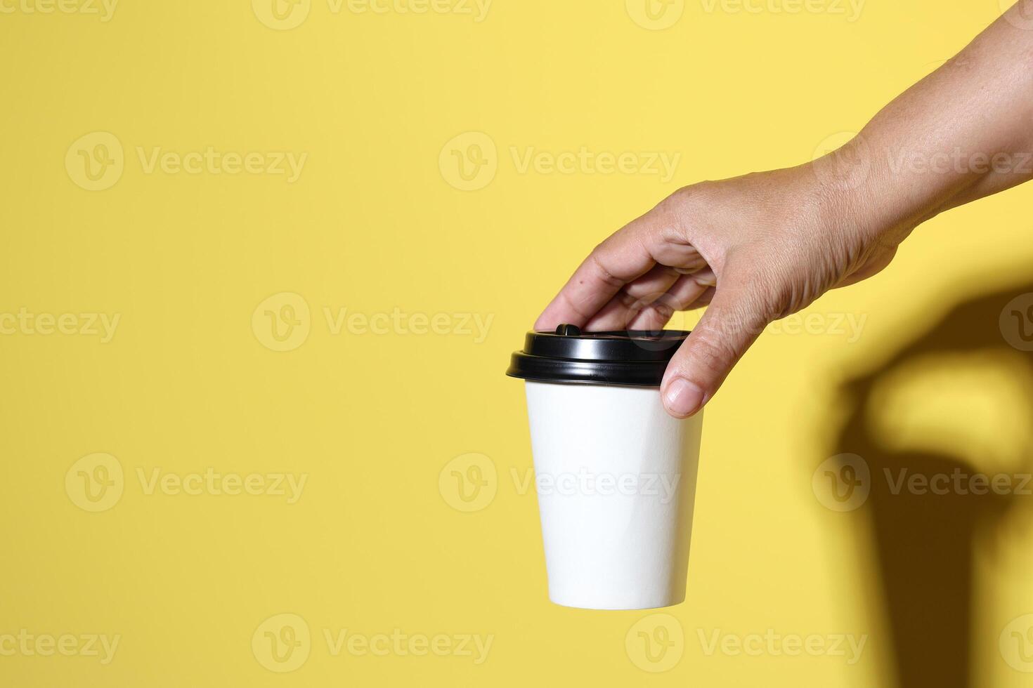 Hand Holding Coffee Papercup on Yellow Background photo