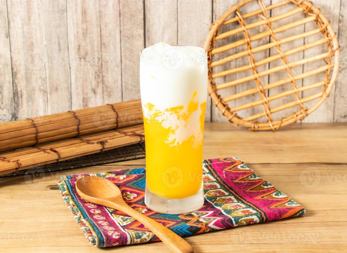 Creamy Mango Milk iced Tea filled with ice cubes served in tall glass isolated on napkin side view on wooden table of taiwan drink photo