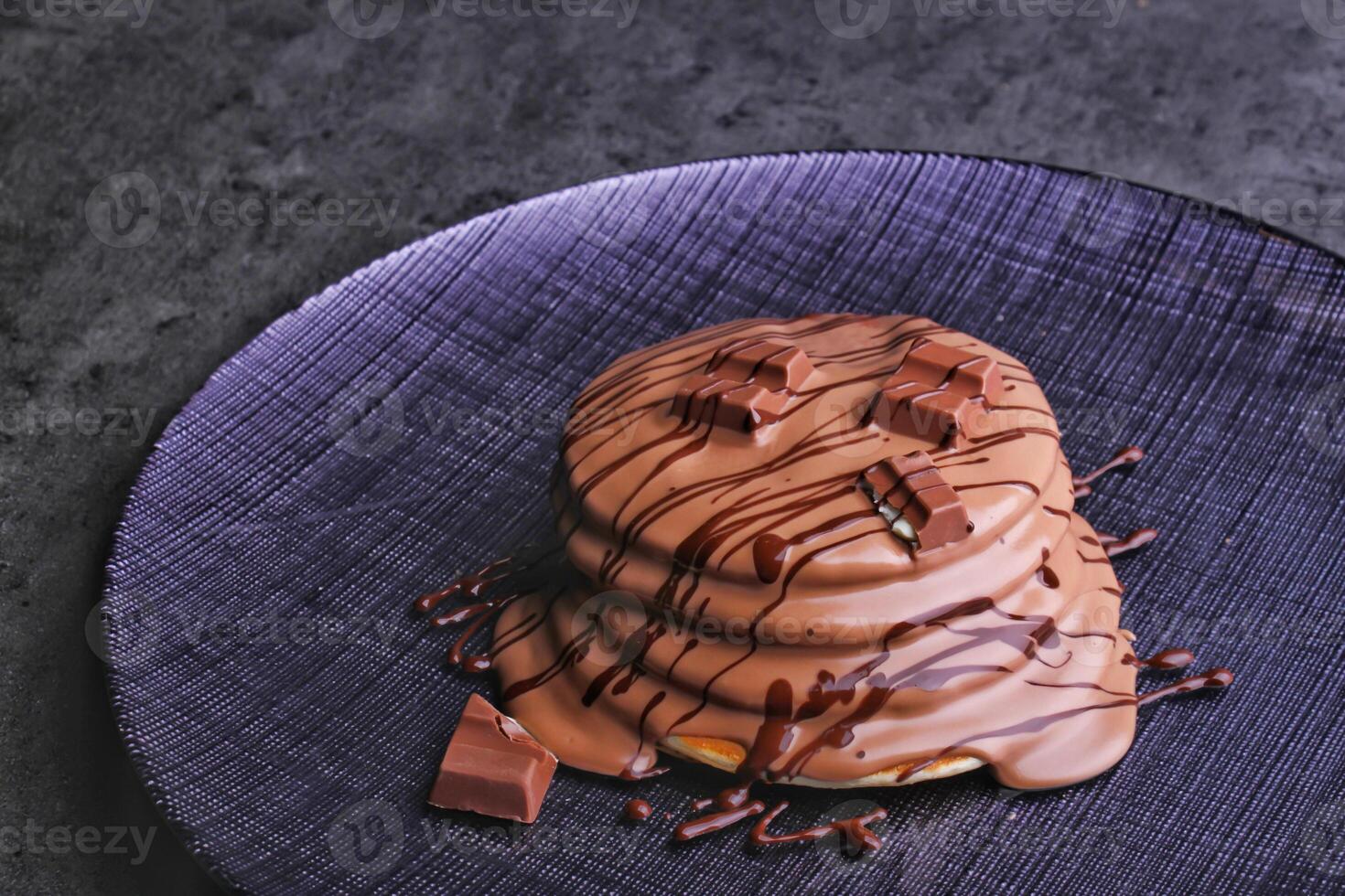 Kinder Chocolate Pancake Stack drizzled with rich chocolate sauce and topped with chocolate chunks served in plate isolated on napkin side view of dessert photo